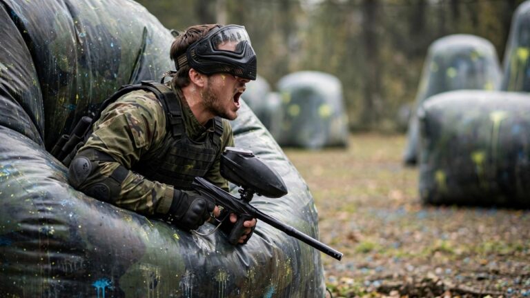 Paintball player shouting a callout to a teammate from behind a bunker mid-game