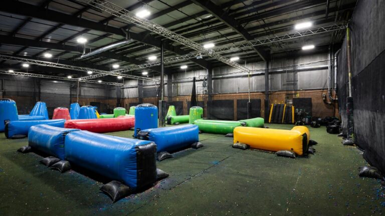 Indoor paintball arena with colorful inflatable bunkers under bright overhead lights